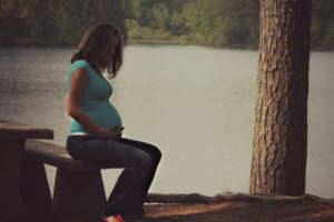 Pregnant woman sitting on outdoor bench, thinking