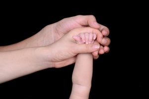 A mother and father's hands holding a newborn's hand.