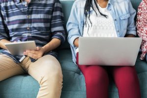 A man and woman sitting on a couch together, each looking at their own computers sitting on their laps.