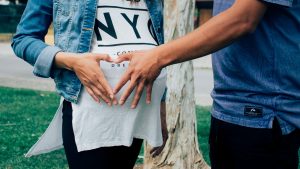 A man and a pregnant woman join hands to form a heart over her stomach.