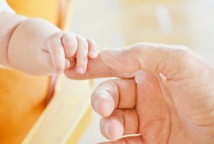 Baby hand reaching out and grabbing the index finger of a male hand.