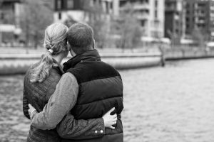 A man and a woman embrace each other as they look out toward the water.