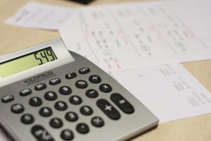Calculator sitting next to several pieces of paper with numbers jotted down.