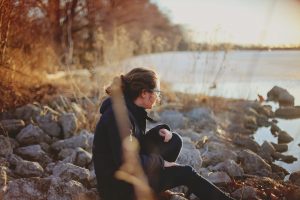 Woman sitting on rocks overlooking the water, thinking about life after adoption