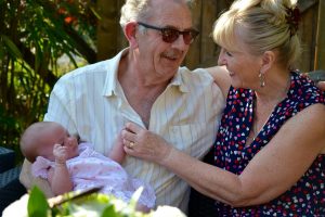 Grandparents sitting arm-in-arm holding a baby.