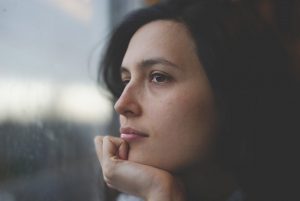 Close up of woman resting her head on her hand and looking out a window.