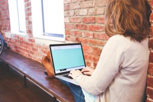 Woman sitting on a bench with a laptop on her lap.