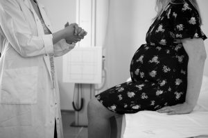 Pregnant woman sits in hospital room discussing her adoption plan with the doctor.