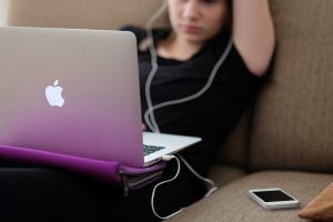 woman wearing black and sitting on a couch with her Apple laptop on her lap and her iPhone sitting next to her.