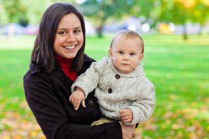 The benefits of open adoption - a birth mother with long dark hair and a black coat holding her baby wearing a grey sweater.