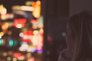 Post Adoption Depression Syndrome Blog Image: A young woman looking out a window. The lights outside are a blurr.