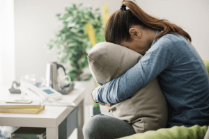 Coping with Life After Adoption. A young woman sits on a couch with her face buried in a pillow.